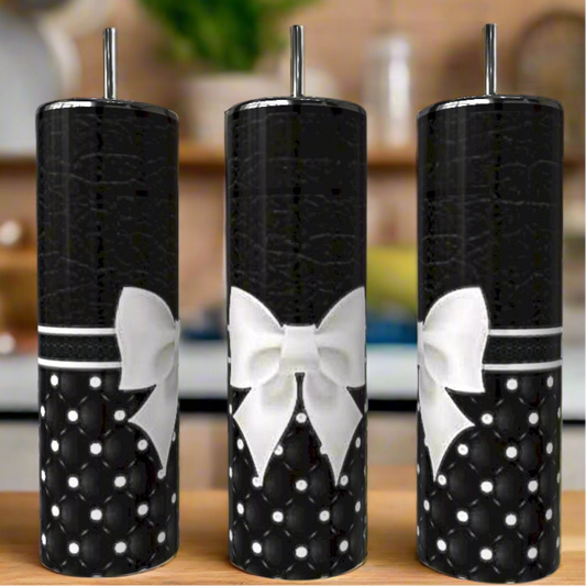 Three Monogram Textured Bow 20oz Skinny Tumblers by Kreative Kreationz, featuring a black quilted pearl pattern, white bows, and metal straws, are displayed side by side on a wooden surface with a blurred kitchen in the background.