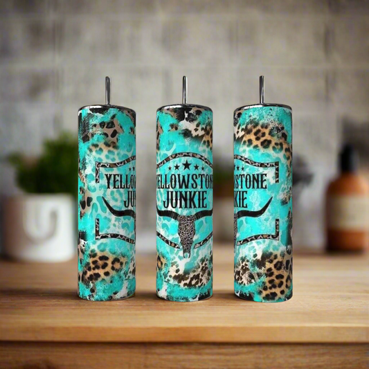 The Kreative Kreationz Teal 20oz Tumbler features a bull skull graphic shown on a wooden surface alongside brown and leopard-print stainless steel tumblers; the background is softly blurred.