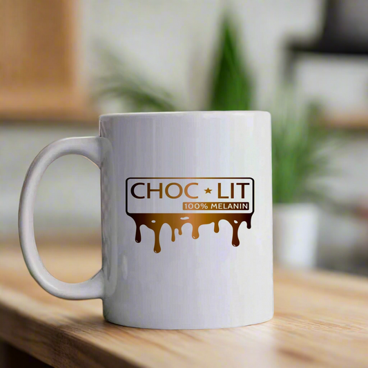 The Choc-Lit Mug by Kreative Kreationz, a white ceramic coffee mug with "CHOC * LIT 100% MELANIN" and dripping chocolate graphics, sits dishwasher safe on wood before a blurred green plant.