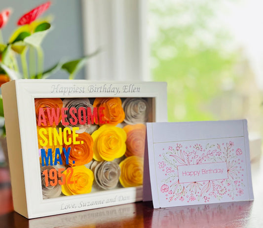 The Kreative Kreationz "Awesome Since | Multicolor Flower Shadow Box" with handcrafted blooms and bold text is showcased next to a pastel floral “Happy Birthday” card, both reflecting beautifully on a glossy surface.