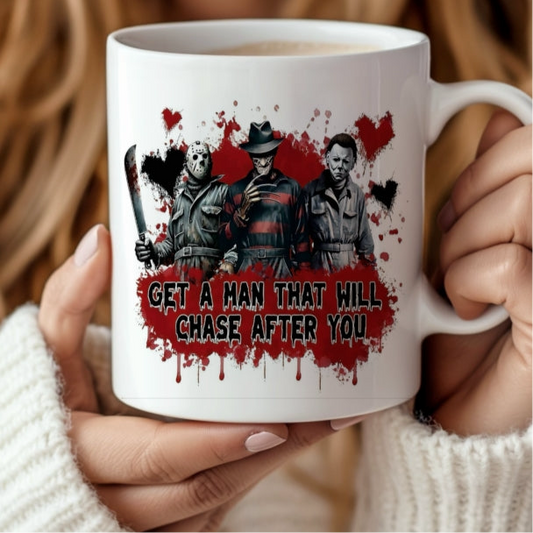 A person holds the "Get a man who will chase after you" Halloween Ceramic Mug by Kreative Kreationz, featuring three horror characters with weapons, a splattered red background—perfect for spooky coffee moments.