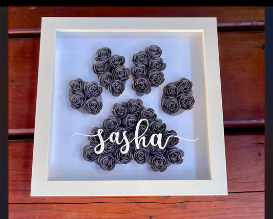 The Paw Print Shadow Box | Personalized by Kreative Kreationz features black paper roses forming a paw print on white, with your pet's name in elegant script on the glass—a unique and personal tribute.