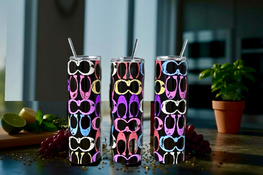 Three colorful tumblers with sunglasses pattern on a table with fruits and a plant in the background.