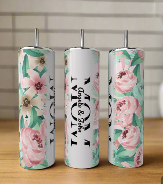 Three tall Kreative Kreationz MOM 20oz Tumblers with pastel floral designs rest on a wooden surface. The center tumbler reads "MOM" and "Angela & John" in black; the others feature only the floral pattern.