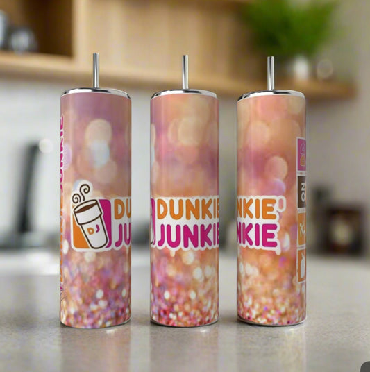 Three Kreative Kreationz Dunkin Junkie 20oz Tumblers with reusable straws sit on a counter. Each features a pink, orange, and white gradient design, “DUNKIN JUNKIE” text, and a coffee cup graphic for a fun touch.