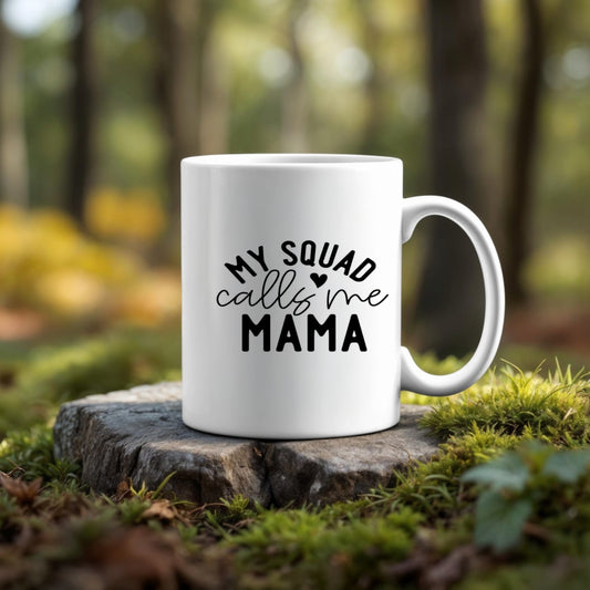 The Kreative Kreationz Mom Squad Mug, featuring "My squad calls me Mama," sits on a tree stump outdoors, perfect for your favorite hot drink and surrounded by green moss with trees blurred in the background.