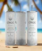 Two cans of Kreative Kreationz Ciroc 20oz Tumbler with 3D Lid Topper are shown on a wooden surface, reminiscent of travel tumblers. The left can is Red Berry flavor, topped with ice and a cherry. The right can is Vodka Snap Frost flavor, topped with ice and a lemon slice. Both cans feature product information and branding.