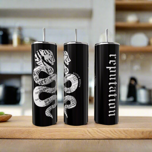 Three black 20oz Look What You Made Me Do skinny tumblers by Kreative Kreationz with silver lids and straws sit on a counter—two with white snake and newspaper designs, the third featuring "reputation" in bold white text. Blurred shelves are behind.