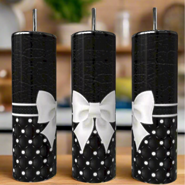 Three Monogram Textured Bow 20oz Skinny Tumblers by Kreative Kreationz, featuring a black quilted pearl pattern, white bows, and metal straws, are displayed side by side on a wooden surface with a blurred kitchen in the background.