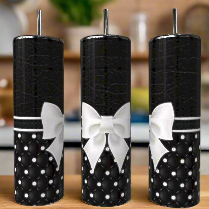 Three Monogram Textured Bow 20oz Skinny Tumblers by Kreative Kreationz, featuring a black quilted pearl pattern, white bows, and metal straws, are displayed side by side on a wooden surface with a blurred kitchen in the background.