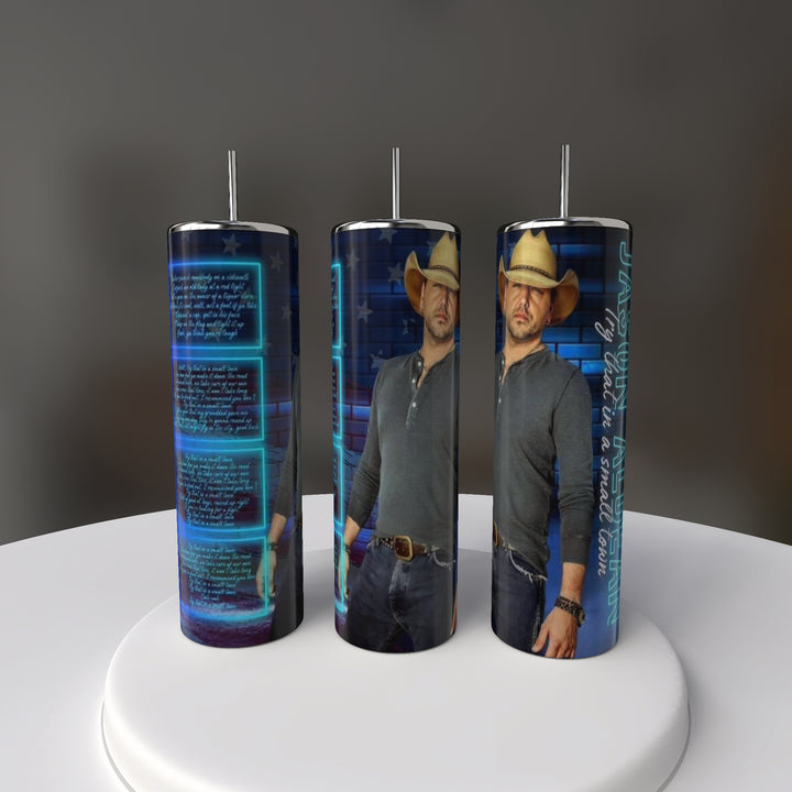 Set against a dark background, the Jason Aldean 20oz Tumblers by Kreative Kreationz display a man in a cowboy hat, gray shirt, and jeans with blue digital text and graphics. These eco-friendly stainless steel tumblers feature an exclusive design.