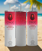 Two cans of Kreative Kreationz Ciroc 20oz Tumbler with 3D Lid Topper are shown on a wooden surface, reminiscent of travel tumblers. The left can is Red Berry flavor, topped with ice and a cherry. The right can is Vodka Snap Frost flavor, topped with ice and a lemon slice. Both cans feature product information and branding.