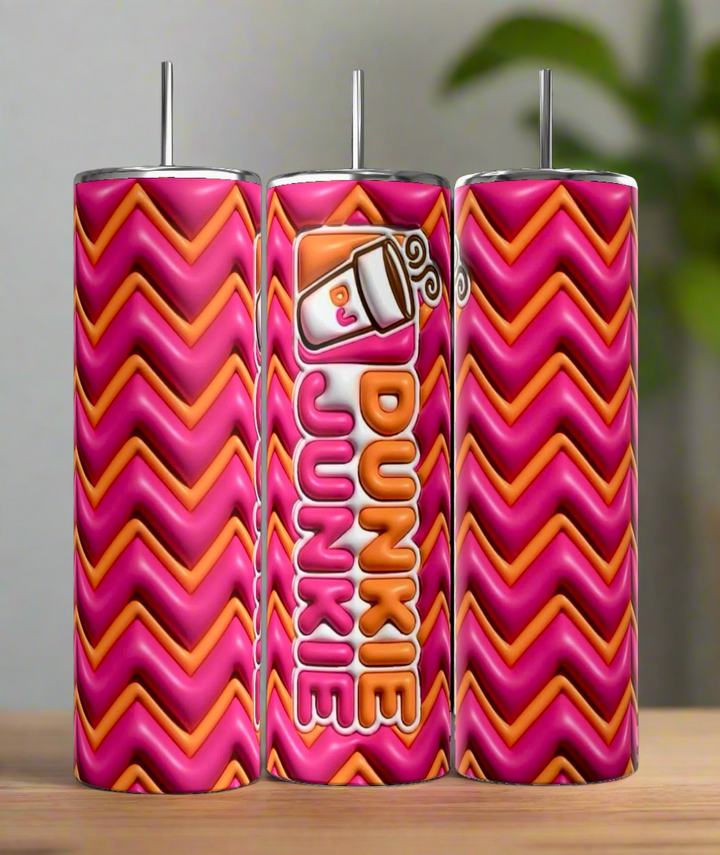 Three Kreative Kreationz Dunkin Junkie 20oz Tumblers, in pink and orange zigzag, stand on wood. The middle tumbler displays a coffee cup graphic with "Dunkie Junkie" text. Each comes with a reusable straw and holds 20 oz of your favorite drinks.