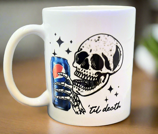 The Kreative Kreationz Pepsi to death Skull Ceramic Mug showcases a grinning skeleton holding a Pepsi can, surrounded by stars, with “‘til death” written below.