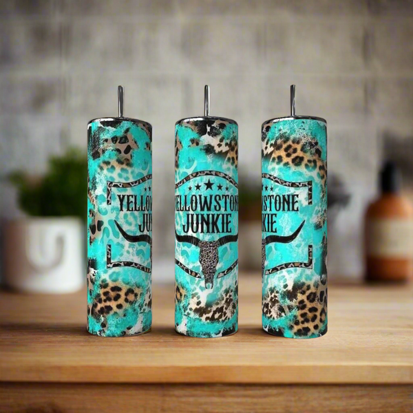 The Kreative Kreationz Teal  20oz Tumbler features a bull skull graphic shown on a wooden surface alongside brown and leopard-print stainless steel tumblers; the background is softly blurred.