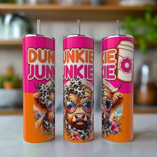 The Kreative Kreationz Dunkin Junkie Cow 20oz Tumbler features a cartoon cow in sunglasses with a leopard-print headband, flowers, and bold "DUNKIE JUNKIE" text on a pink-orange background with donut and coffee cup accents.