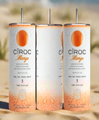 Two cans of Kreative Kreationz Ciroc 20oz Tumbler with 3D Lid Topper are shown on a wooden surface, reminiscent of travel tumblers. The left can is Red Berry flavor, topped with ice and a cherry. The right can is Vodka Snap Frost flavor, topped with ice and a lemon slice. Both cans feature product information and branding.