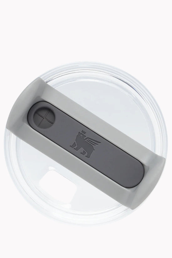 A clear, round plastic lid from a top-down view, featuring a gray sliding cover with a small circular opening on one side. The sliding cover has a logo of a winged lion wearing a crown. This customizable Kreative Kreationz Taylor Swift 1989 Taylor’s Version 20, 30, 40 ounce Stanley Lid Plate/Topper is perfect for adding flair to your drinkware collection.