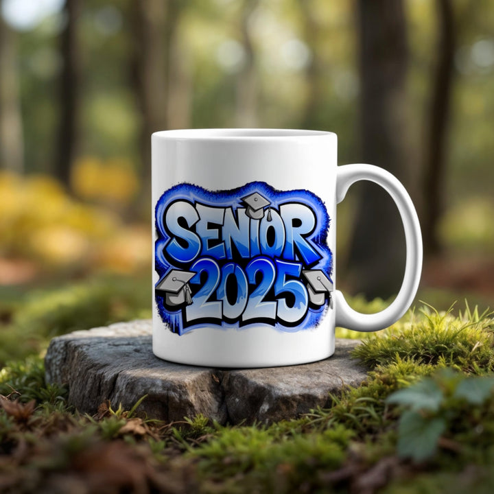 The Class Of 2025 Graduate Mug by Kreative Kreationz features blue graffiti-style text and graduation caps, displayed on a tree stump outdoors—an ideal graduation gift with a forest backdrop.