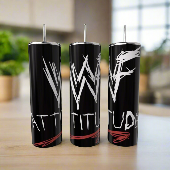 Three black Kreative Kreationz WWF Attitude 20oz Tumblers with silver straws sit on a countertop. Each features "WWF ATTITUDE" in a bold white graffiti-style font with red accents. A blurred kitchen is visible in the background.