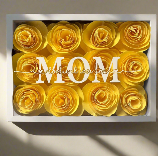 The Mom 5x7 Flower Shadow Box by Kreative Kreationz features yellow paper roses surrounding "MOM" in bold white letters with "love u, I love you" in cursive—a unique keepsake for any mom.