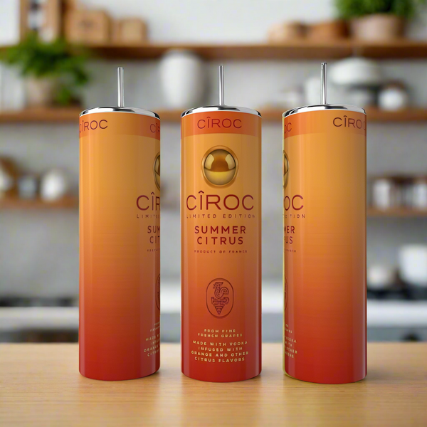 Three tall, slender Kreative Kreationz Summer Citrus 20oz Tumblers with eco-friendly stainless steel straws are displayed on a wooden surface. The orange and gold gradient tumblers stand out against a blurred kitchen background.