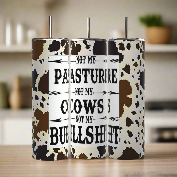 Three Kreative Kreationz "Not my Pasture, Not My Cows Not My BS" 20oz stainless steel tumblers with cow print and stainless steel straws rest on a kitchen counter, each boldly displaying the custom phrase in black lettering.