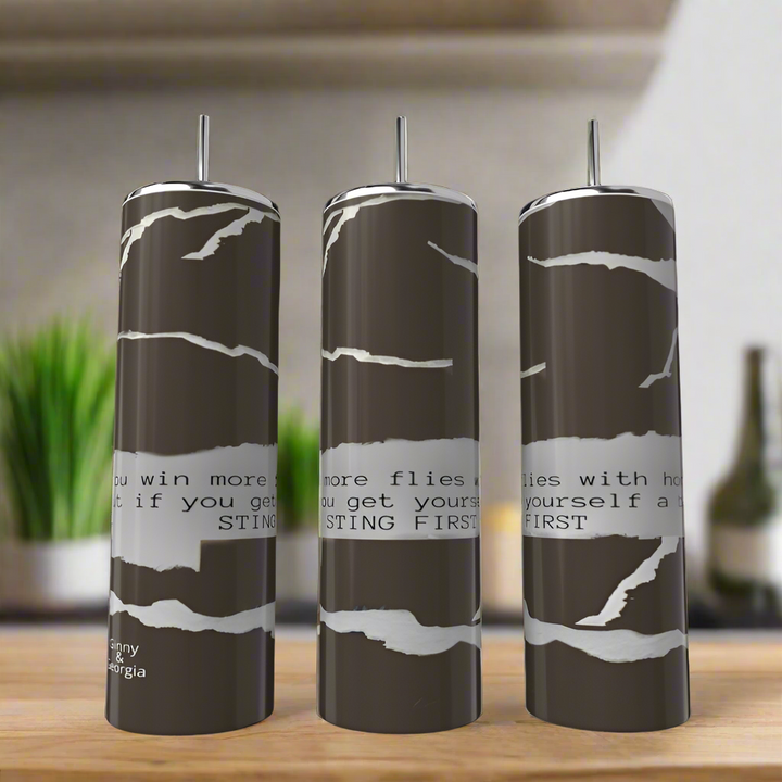 Three dark stainless steel "Sting Like a Bee | Ginny & Georgia" 20oz tumblers by Kreative Kreationz, each with a torn paper design and metal straw, sit on a counter. Visible text: "win more flies... if you get...STING FIRST.
