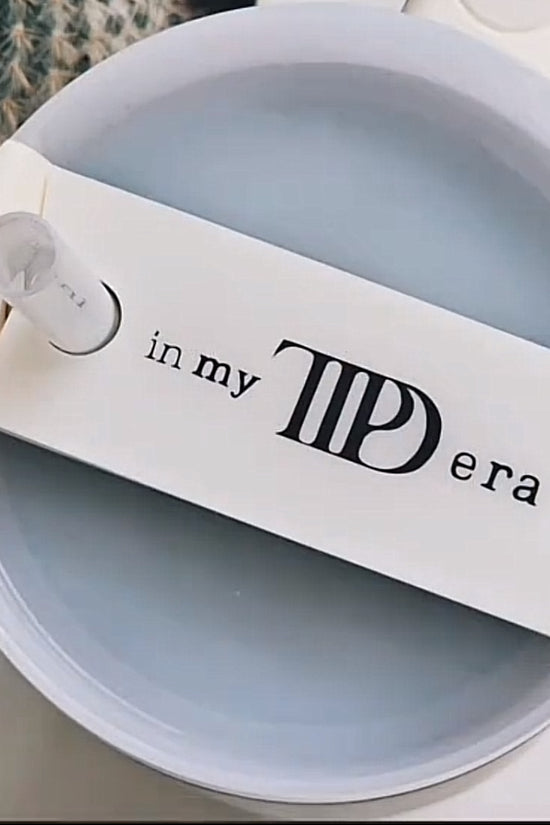 The "In My TTPD Era Tumbler Lid Topper" by Kreative Kreationz features a design that says "in my TID era" with illustrations of flying seagulls around the words. This Swiftie accessory is showcased from the top, clearly displaying its intricate lid topper, and is compatible with Stanley 20, 30, and 40 oz tumblers.