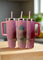 Three pink Kreative Kreationz stainless steel tumblers with handles and straws are displayed on wood. The center "Lover House Taylor Swift Engraved Tumbler" features a house design and "Lover" in cursive, set against a softly blurred background.
