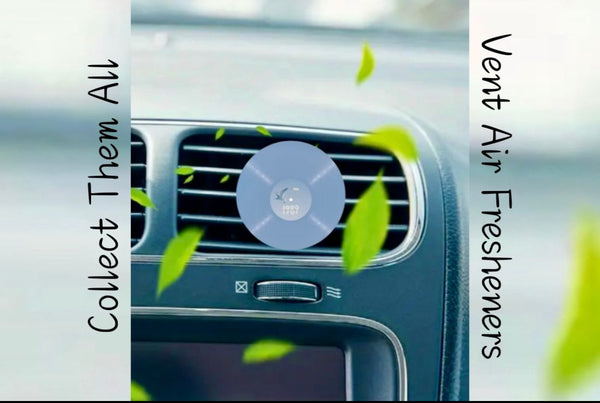 A Taylor Swift Car Air Freshener by Kreative Kreationz, featuring a blue circular vinyl record design, is clipped to a car vent as green leaves blow inside. Side text says, “Collect Them All” and “Vent Air Fresheners.”.