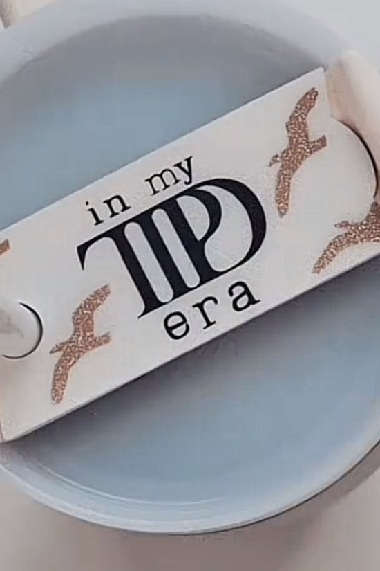 The "In My TTPD Era Tumbler Lid Topper" by Kreative Kreationz features a design that says "in my TID era" with illustrations of flying seagulls around the words. This Swiftie accessory is showcased from the top, clearly displaying its intricate lid topper, and is compatible with Stanley 20, 30, and 40 oz tumblers.