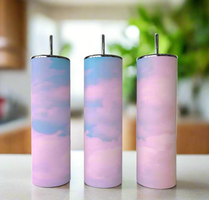 The Kreative Kreationz Love Clouds 20oz Skinny Tumblers feature a pastel pink and blue cloudy sky design with metal straws—eco-friendly and perfect for any occasion. Set of three shown on a white surface in a bright, blurred kitchen.
