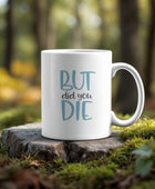 The But Did You Die Point Mug by Kreative Kreationz features "BUT did you DIE" in vibrant colors on a white, dishwasher-safe mug, pictured on a forest tree stump surrounded by moss and sunlight.
