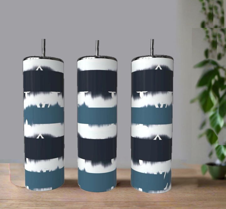 The Kreative Kreationz Teal Stripe 20oz Skinny Tumbler, made of eco-friendly stainless steel, features a metal straw and a blue, navy, and white striped pattern, displayed on wood with a blurred green plant in the background.