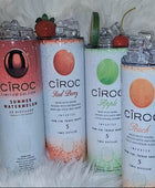 Two cans of Kreative Kreationz Ciroc 20oz Tumbler with 3D Lid Topper are shown on a wooden surface, reminiscent of travel tumblers. The left can is Red Berry flavor, topped with ice and a cherry. The right can is Vodka Snap Frost flavor, topped with ice and a lemon slice. Both cans feature product information and branding.